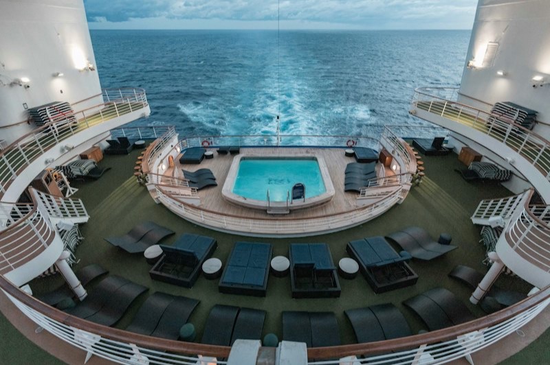 La piscine du pont arrière d'un navire de croisière, entourée de transats, face au sillage en pleine mer