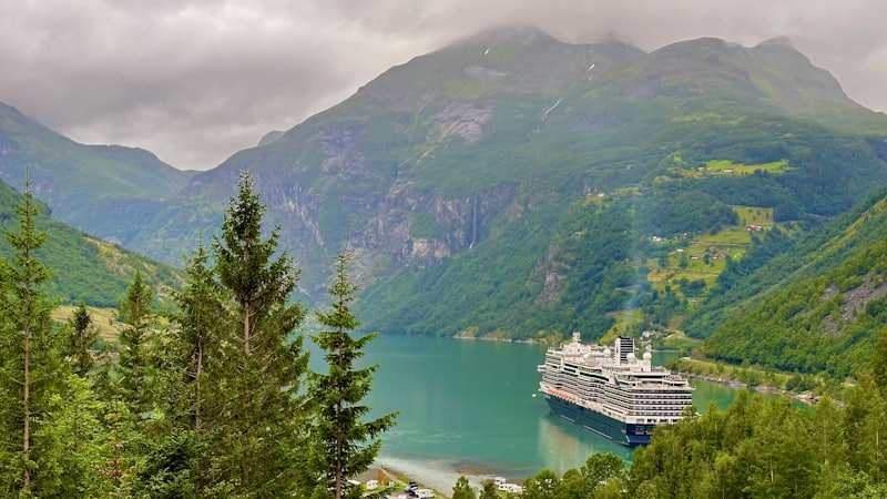 Navire de croisière à quai au fond d'un fjord norvégien bordé de montagnes boisées